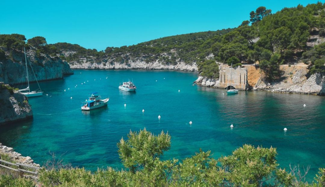 Calanque de Provence avec eau turquoise encadrée de falaises calcaires et de pins, bateaux ancrés