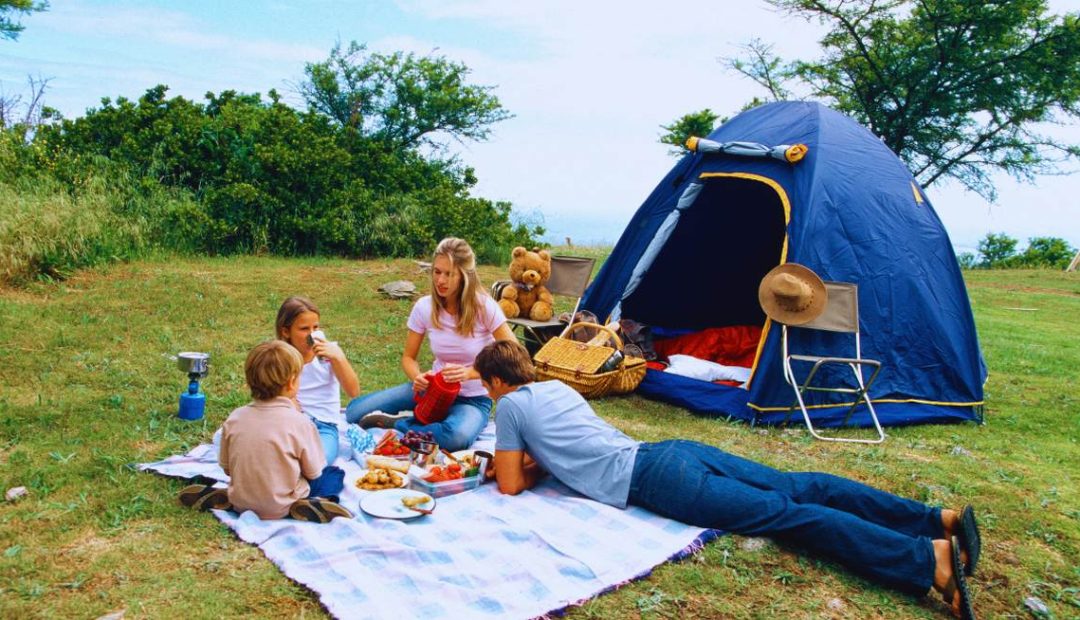 Famille avec enfants profitant d'un pique-nique au camping devant leur tente dans la nature