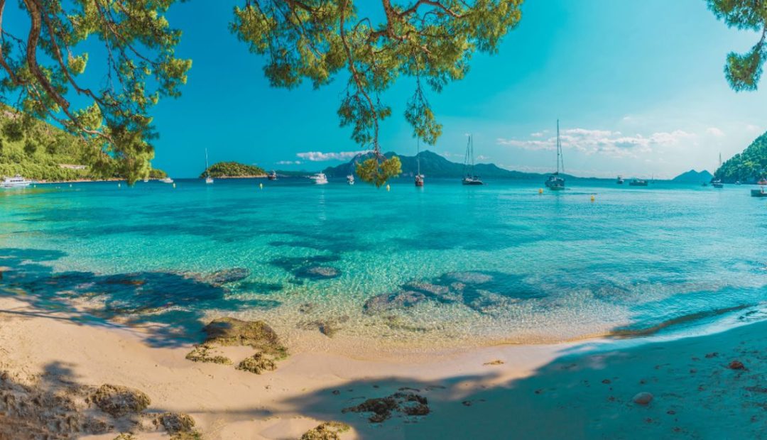 Plage de Majorque avec eaux turquoise, bateaux et pins en bord de mer