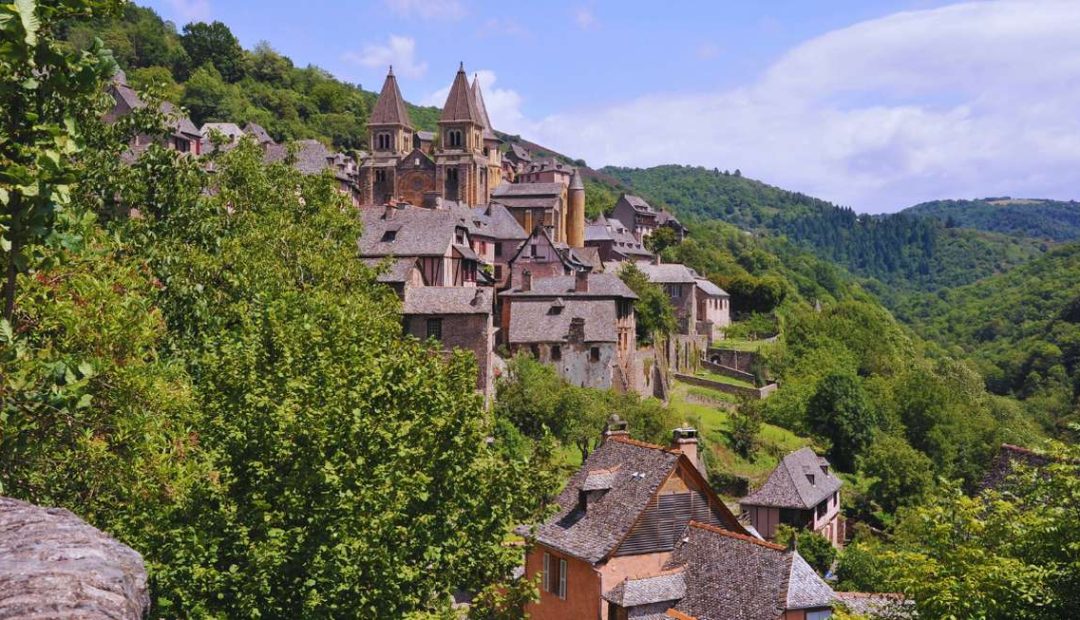 Village médiéval perché sur une colline en France avec église et maisons à toits de pierres entourés de collines boisées