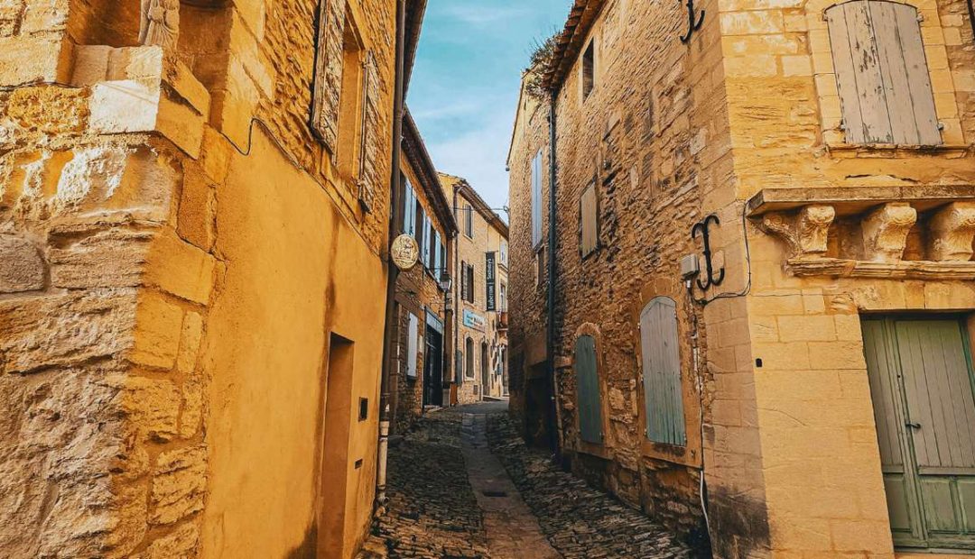 Rue etroite en pierre doree d'un village provencal perche avec volets colores et calade pavee