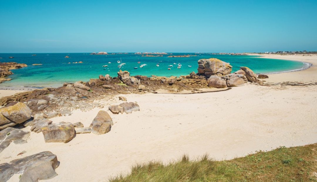 Plage de sable blanc bordée de rochers de granit et d'eau turquoise en Bretagne